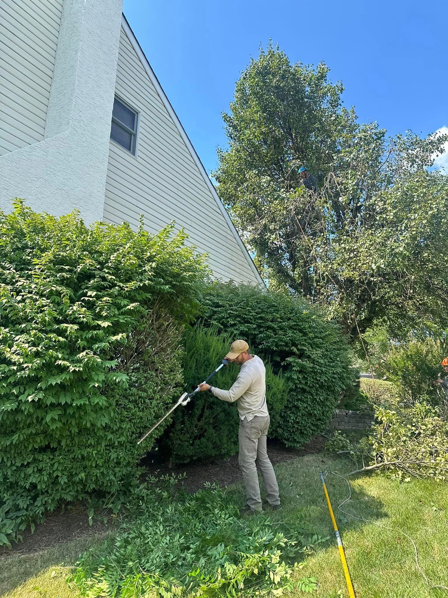 A man is spraying a hedge with a hose in front of a building.