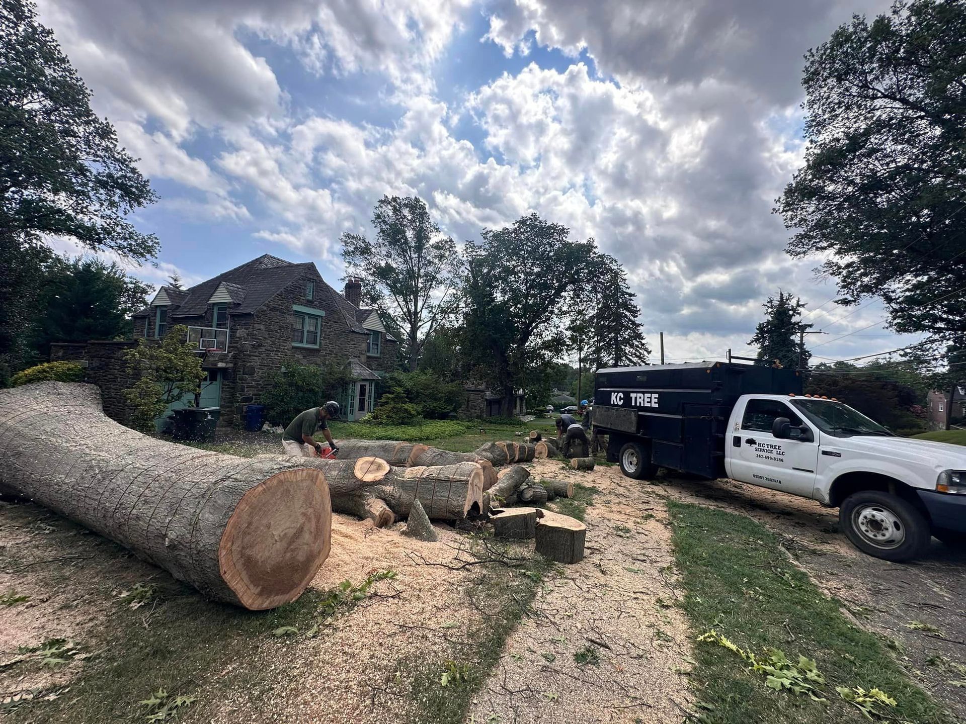 A white truck is parked next to a large log in front of a house.