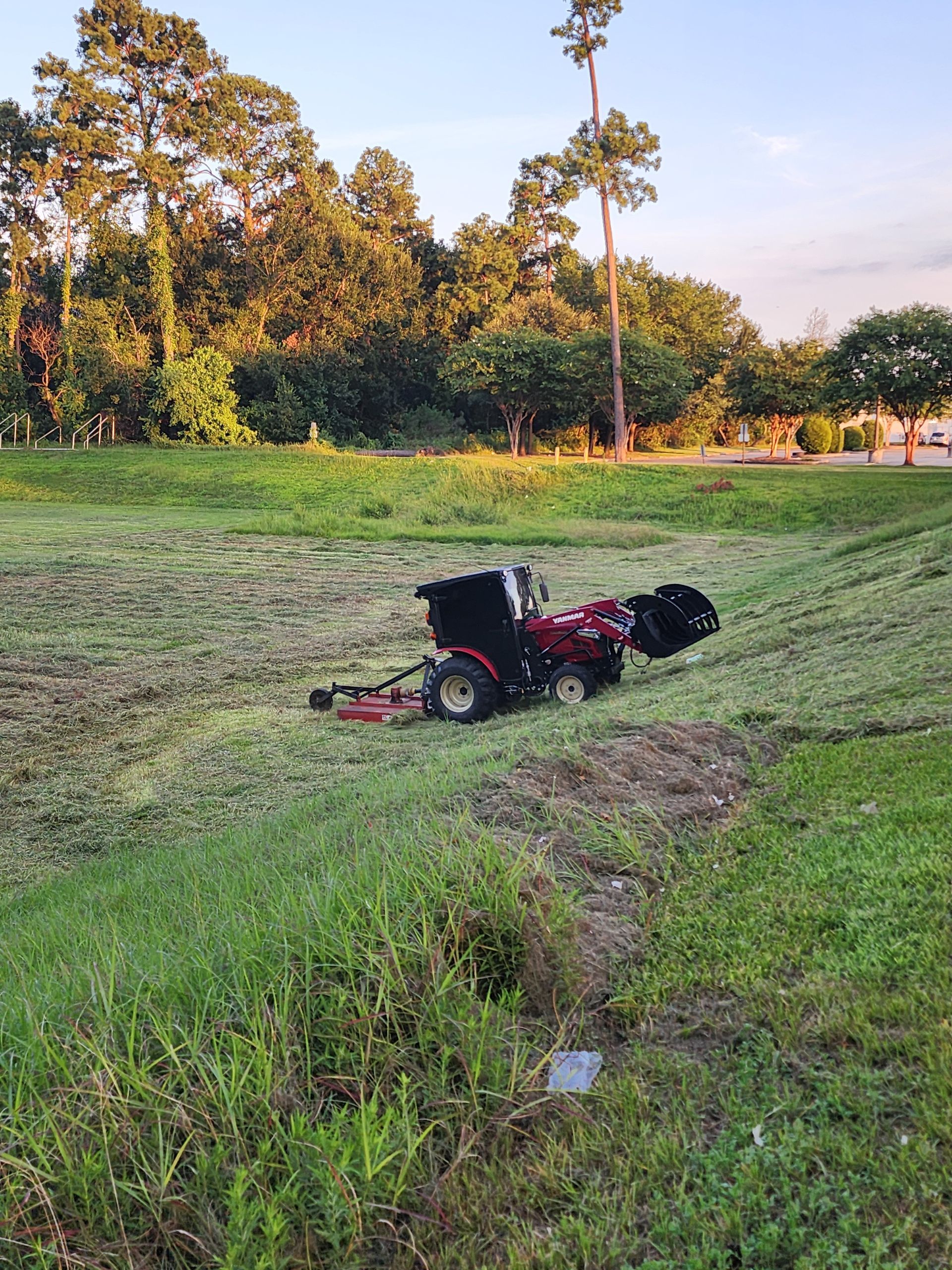A dog is sitting on a lawn mower in a field.