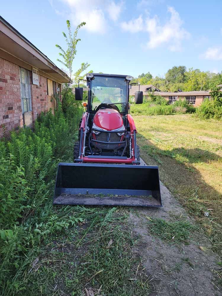 A red tractor is parked in a grassy field next to a house.