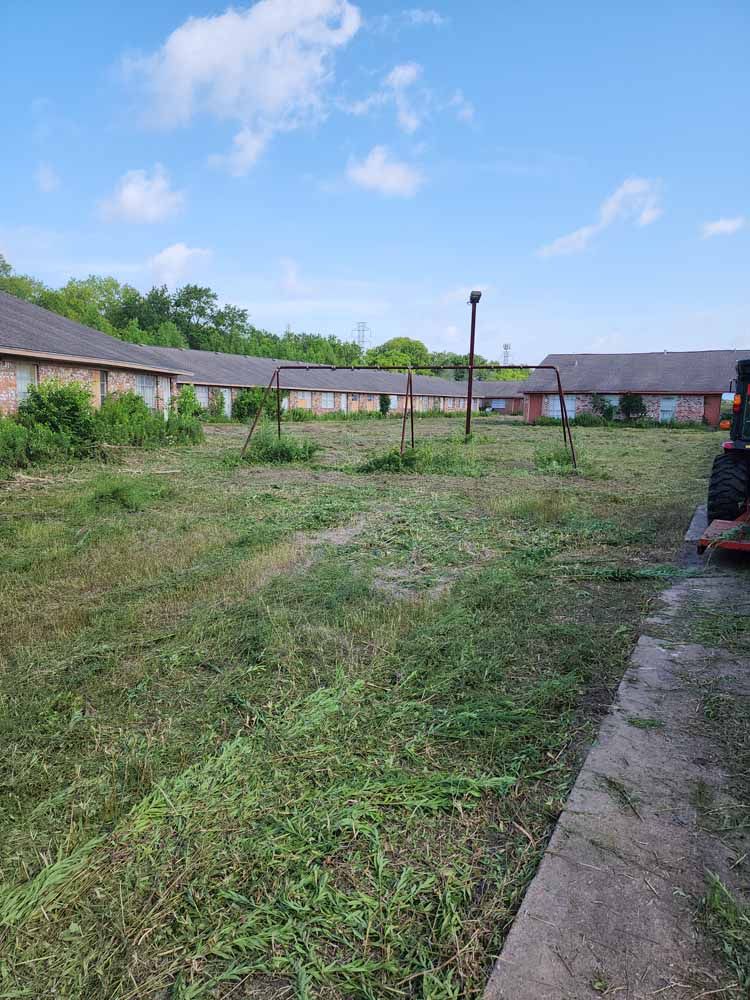 A person is mowing a large grassy field in front of a building.