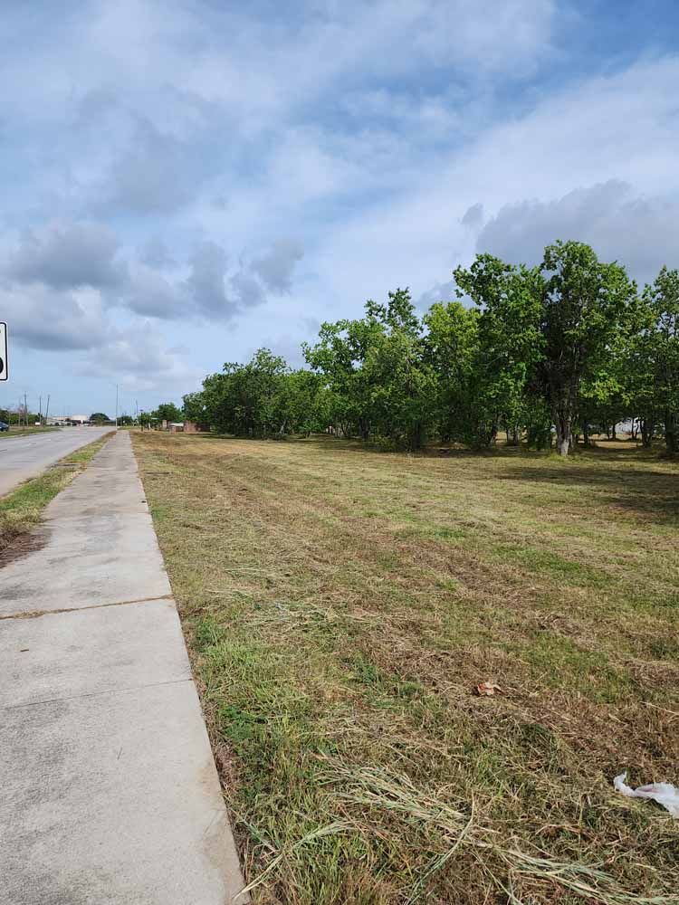 A concrete sidewalk runs through a grassy field next to a road.