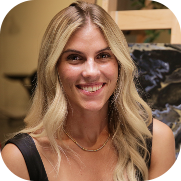 Woman with blonde hair smiling, wearing a black top and a gold necklace.