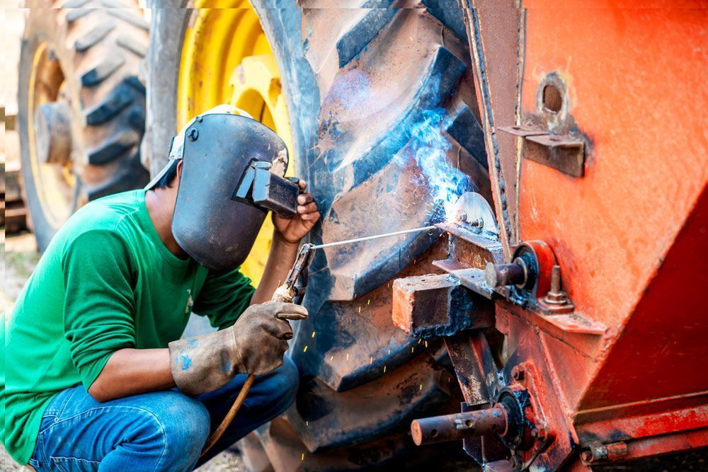 A Man Wearing A Welding Mask Is Welding A Tire On A Tractor — Agriweld Engineering in Dubbo, NSW