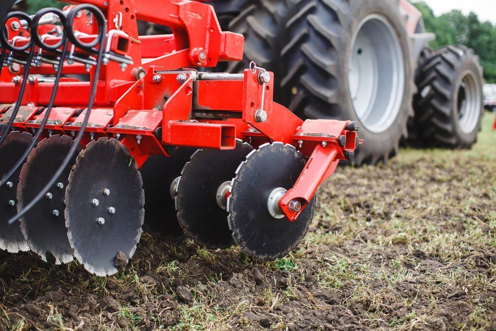 A Red And Black Tractor Is Ploughing A Field — Agriweld Engineering in Dubbo, NSW