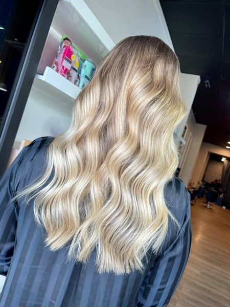 Woman With Long, Wavy, Blonde Hair At A Salon, Wearing A Black Smock — Gina T Hair & Beauty In Mackay, QLD