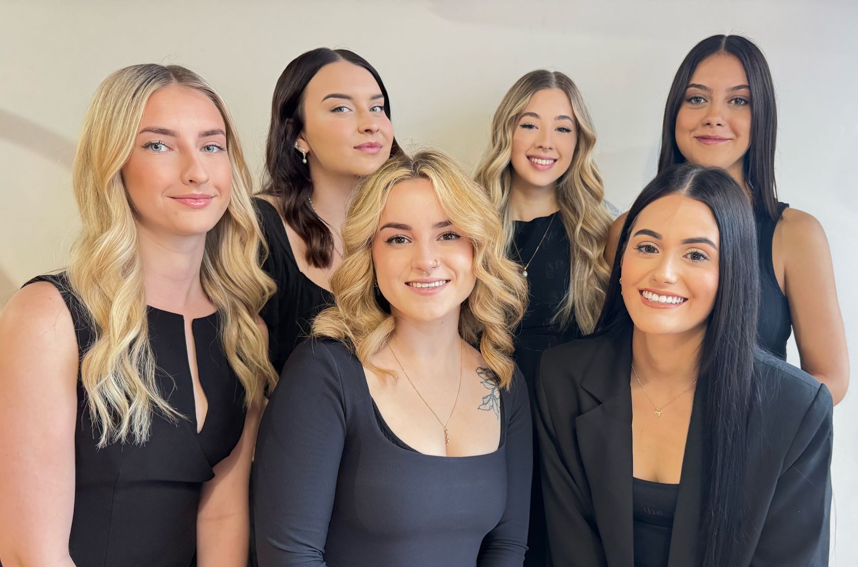 Group of six women posing in front of a white wall, all wearing black — Gina T Hair & Beauty In Mackay, QLD
