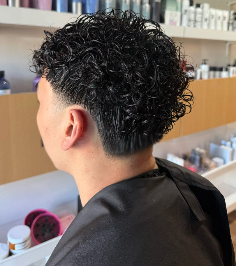 Man with dark curly hair and a faded haircut, sitting in a salon chair.— Gina T Hair & Beauty In Mackay, QLD