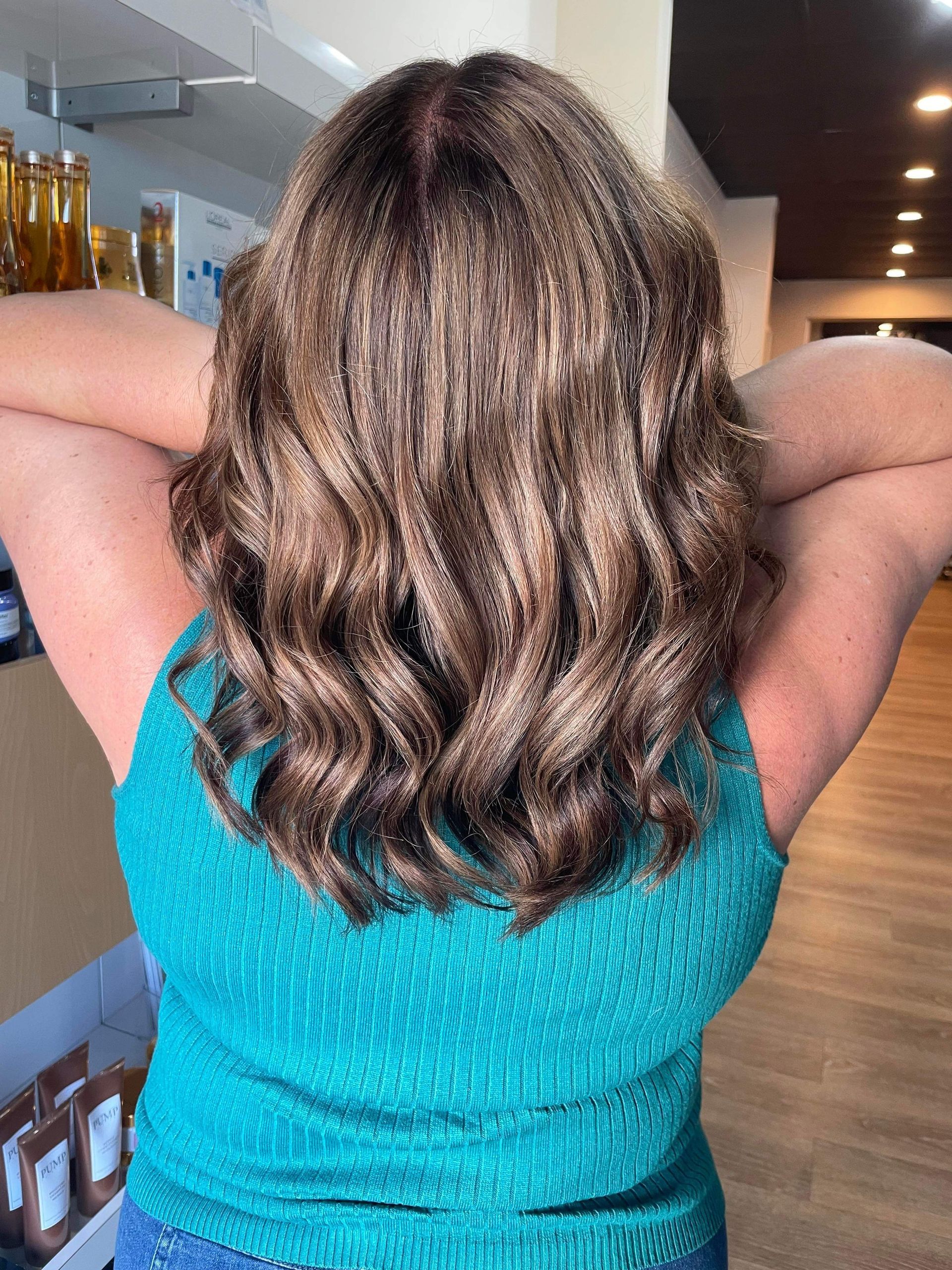 Woman With Wavy, Highlighted Hair Smiles As Stylists Work On Her In A Salon — Gina T Hair & Beauty In Mackay, QLD