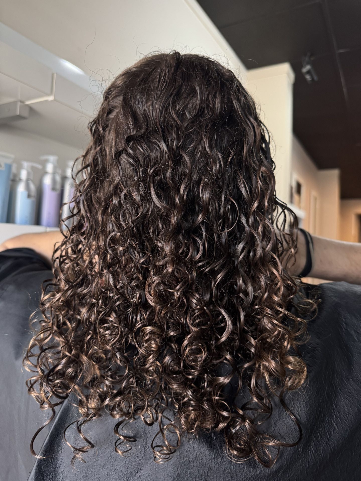 Back view of a person with dark brown curly hair, in a salon setting. Hair is wet and styled.— Gina T Hair & Beauty In Mackay, QLD