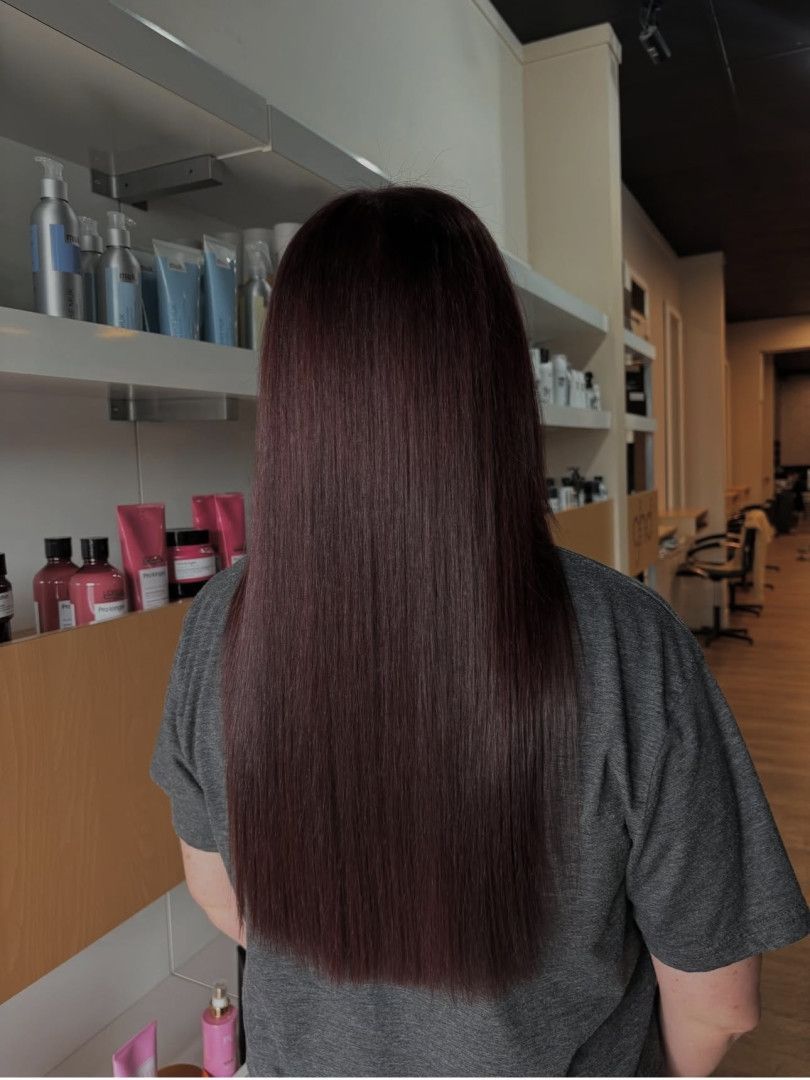 Person with long, straight, dark burgundy hair stands in a salon.— Gina T Hair & Beauty In Mackay, QLD