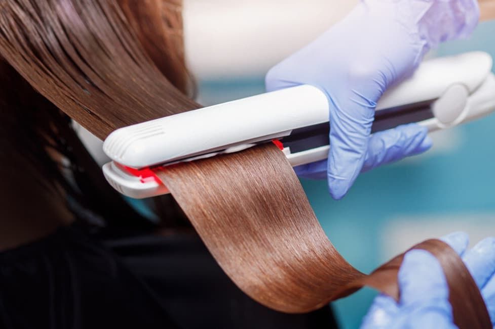 Hair Being Straightened With A Flat Iron, Producing Sleek, Shiny, Brown Strands — Gina T Hair & Beauty In Mackay, QLD