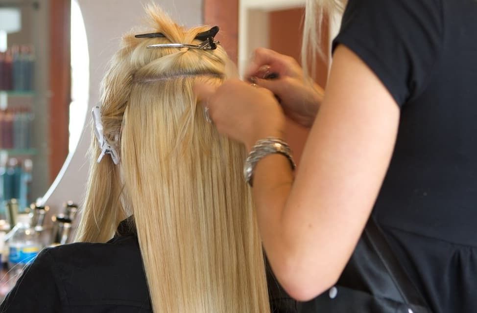 A Stylist Attaching Blonde Hair Extensions To A Client's Hair At A Salon — Gina T Hair & Beauty In Mackay, QLD