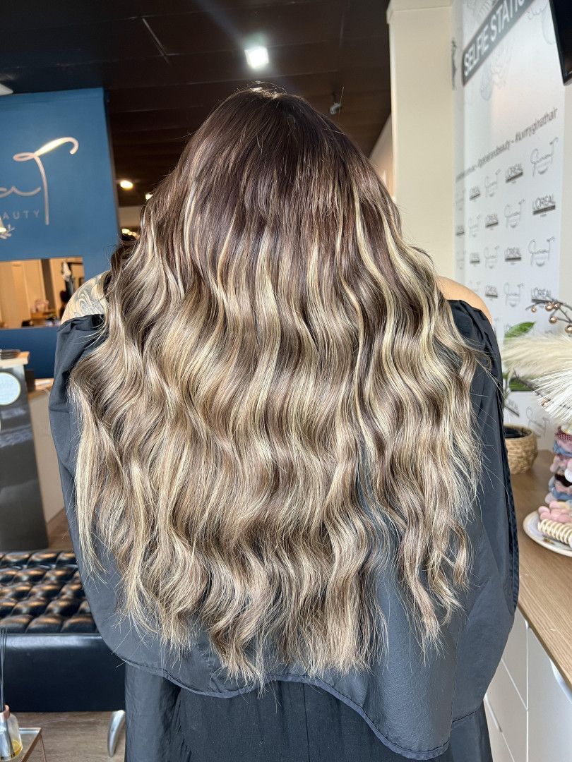 Woman with long, wavy, highlighted brown and blonde hair, in a salon.— Gina T Hair & Beauty In Mackay, QLD