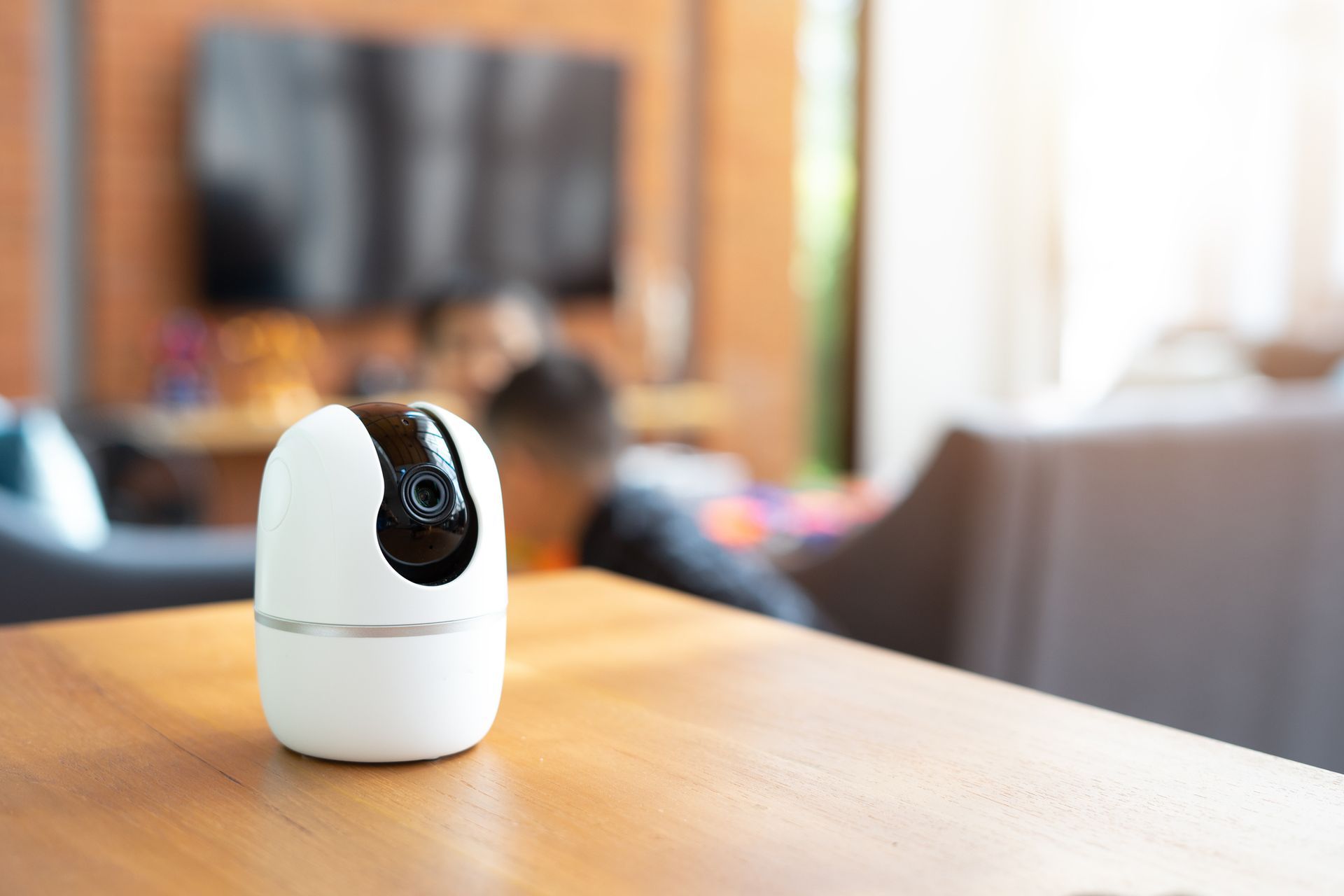 White security camera rests on wooden table near living room TV.