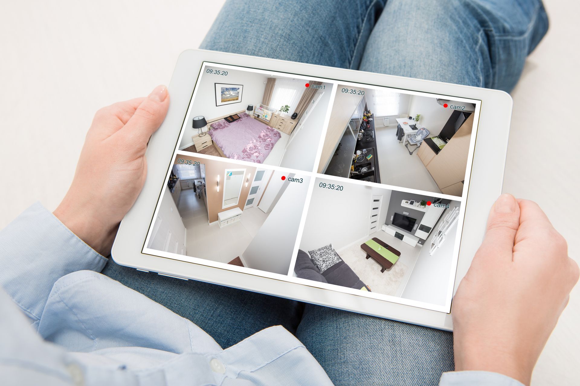 Person holding a tablet showing four camera views of a home's interior.