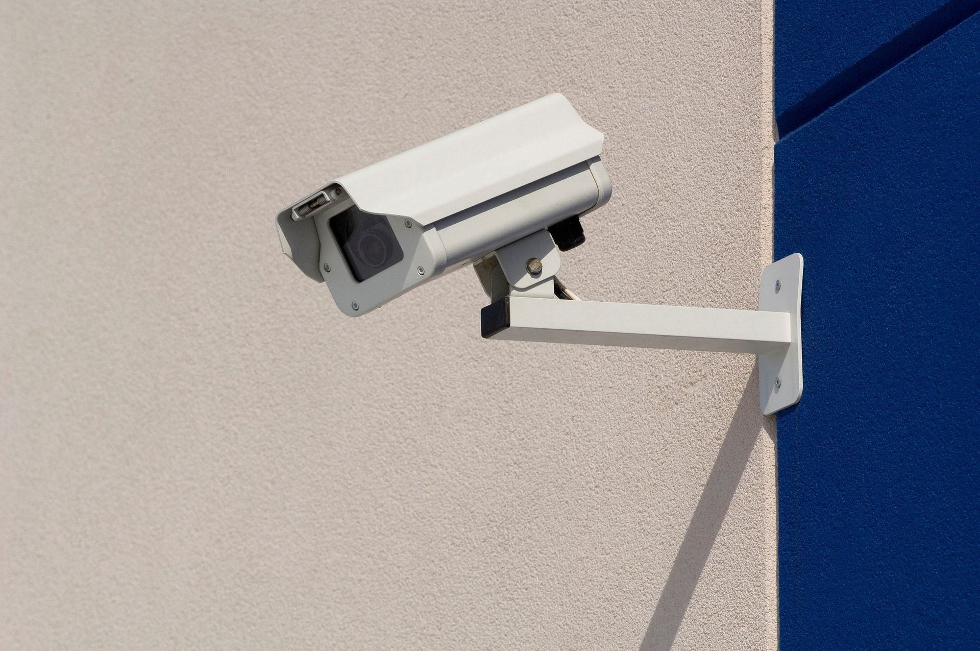 Security camera mounted on a light beige building wall, facing right.