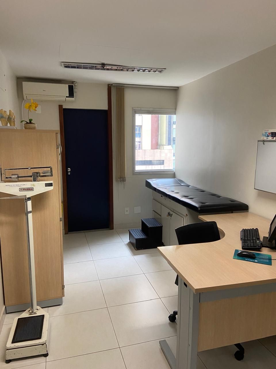 Um consultório médico com mesa, balança e mesa de exame.