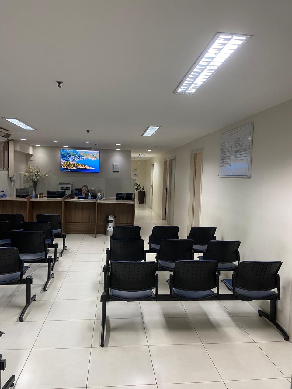Uma sala de espera com fileiras de cadeiras e uma televisão na parede.