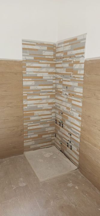 Uomo con equipaggiamento di sicurezza che si cala in corda doppia da un edificio, casco verde, attrezzatura in mano, vista dall'alto.