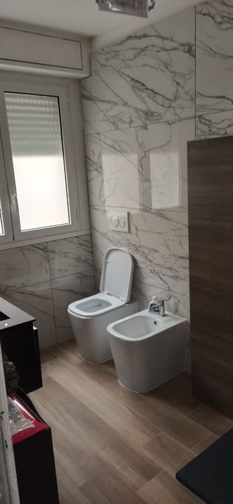 Uomo con equipaggiamento di sicurezza che si cala in corda doppia da un edificio, casco verde, attrezzatura in mano, vista dall'alto.