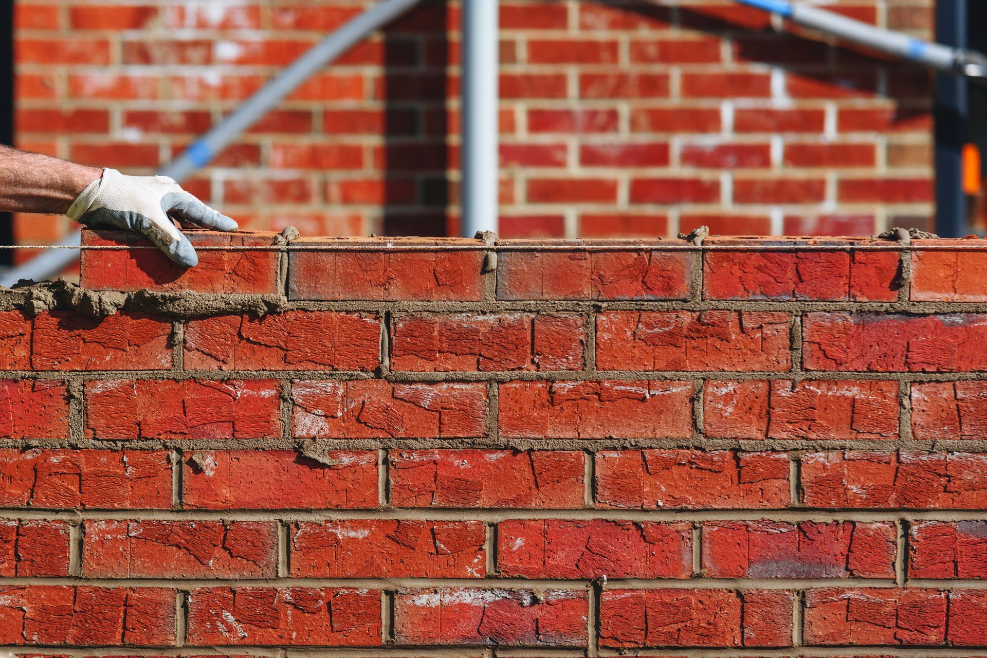 Gloved worker building a red brick wall.