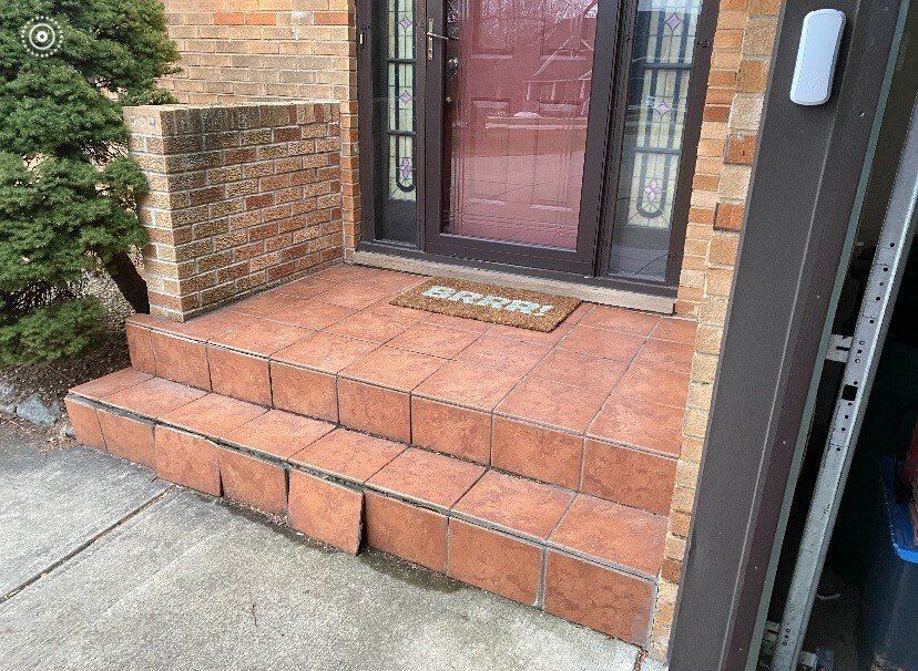 Brick steps leading to a house's front door with a doormat. The steps and surrounding walls are brick-colored.