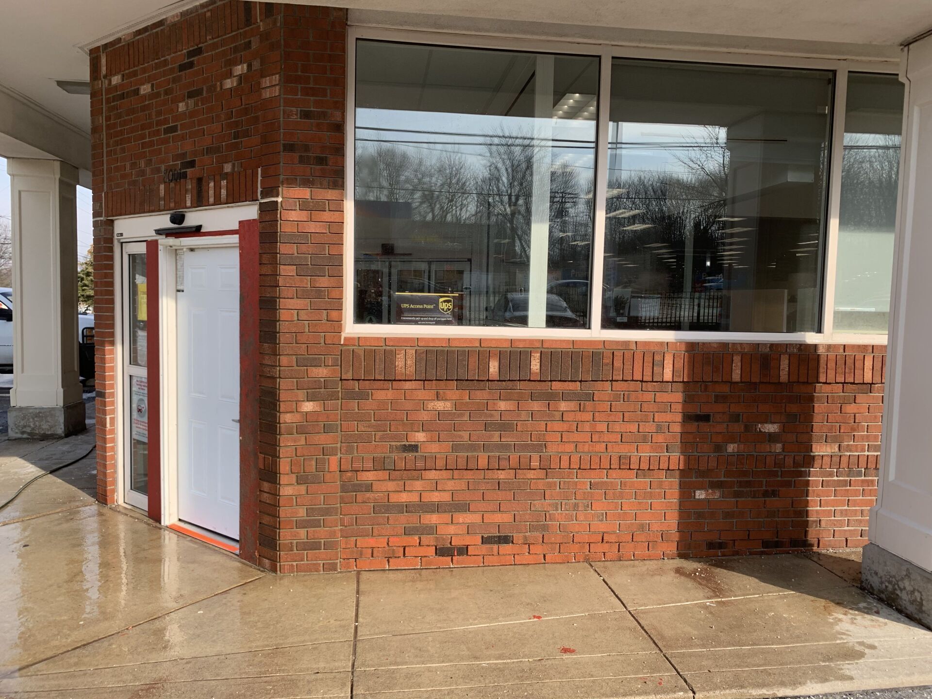 Brick building exterior with a white door, large window, and wet sidewalk.