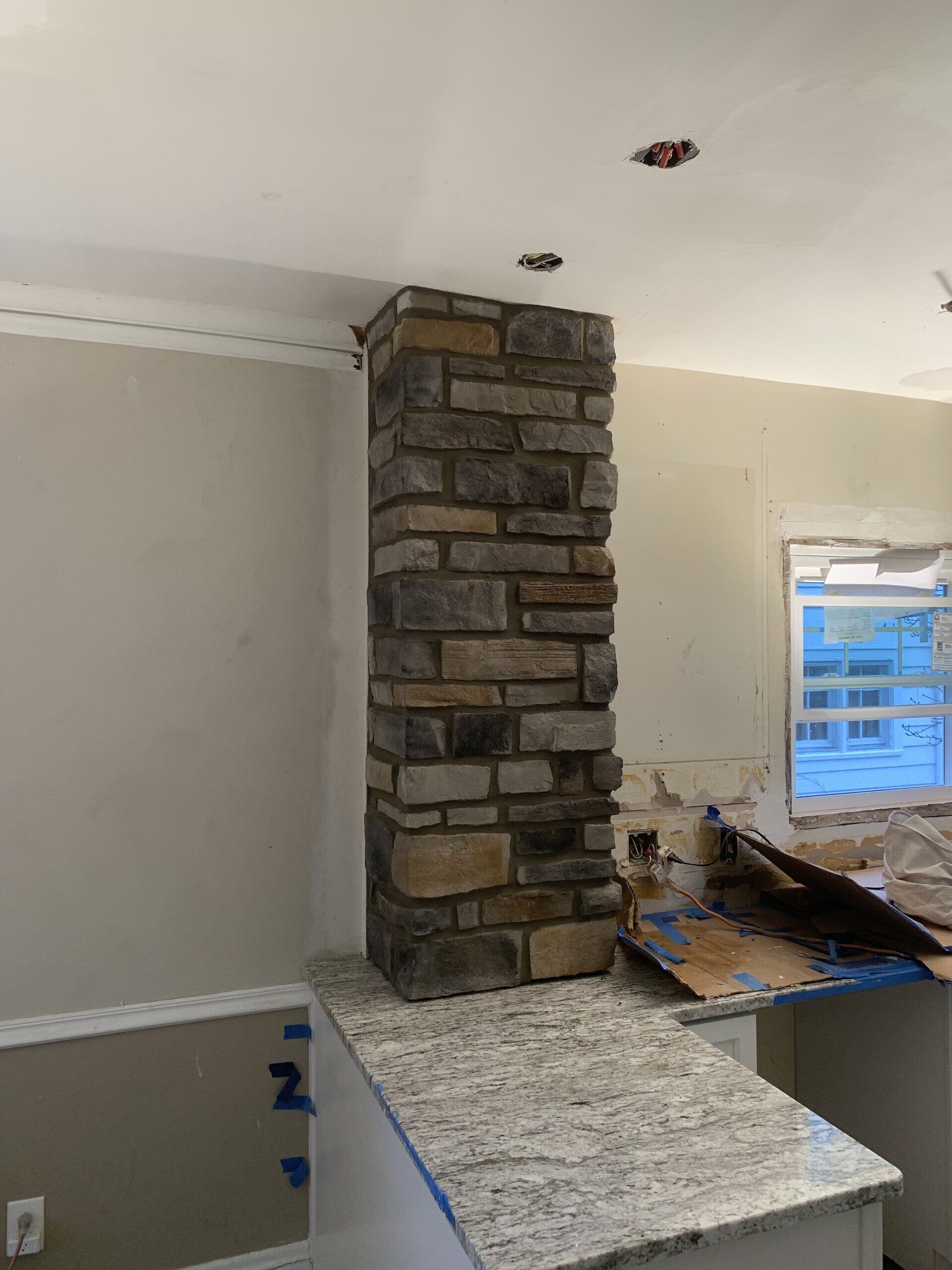 Stone column in a kitchen, placed on a granite countertop. The setting is under construction with unfinished walls and trim.