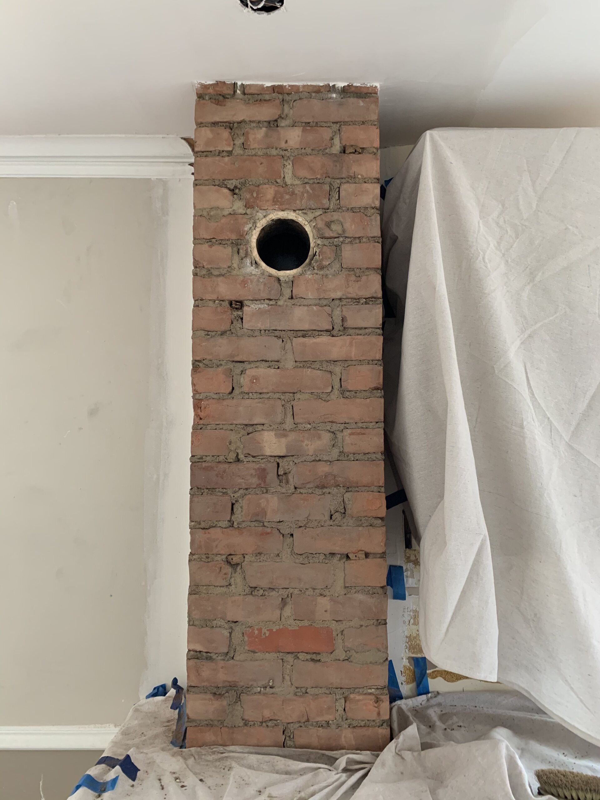 Brick chimney with a circular opening, white ceiling, and protective sheet on the right side.