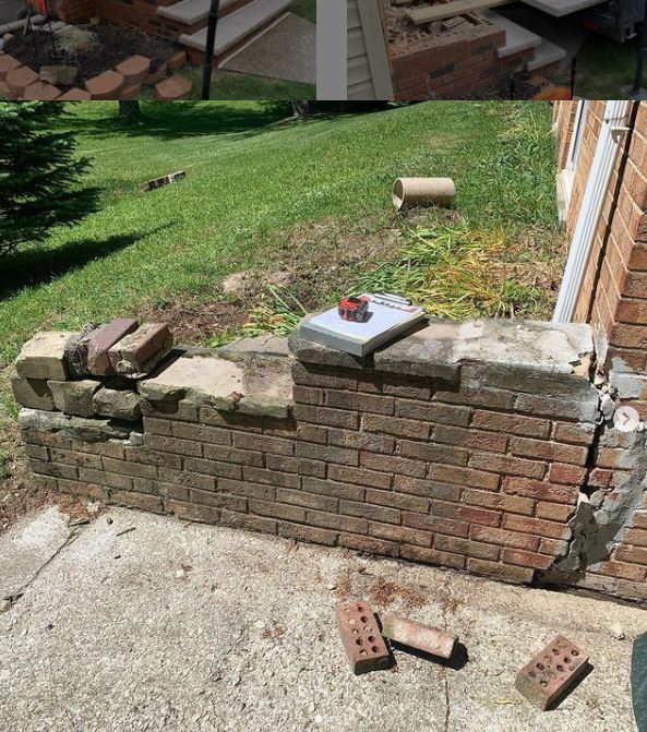 Brick retaining wall in disrepair, with missing bricks, sitting on a concrete patio, near a building and grassy hill.