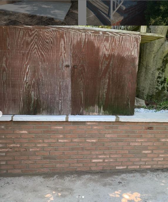 Wooden structure atop a brick wall. The wood is weathered and wet, with green algae at the bottom.