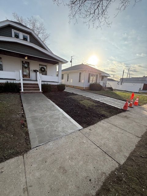 A view from a sidewalk toward two neighboring houses with newly poured concrete walkways and dark mulch beds.