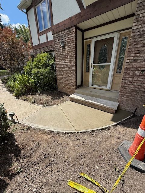 A new curved concrete walkway leading to the front door of a brick home, with a construction cone nearby.