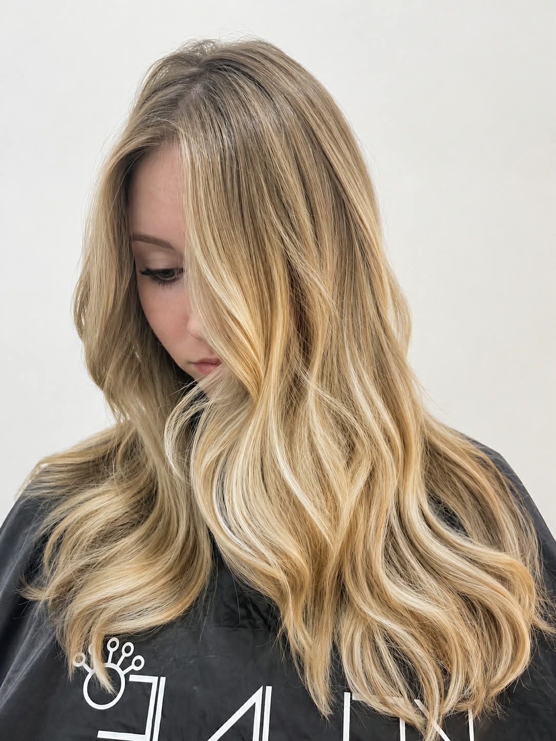 Blonde woman with wavy hair looking down, wearing a black sweatshirt against a light background