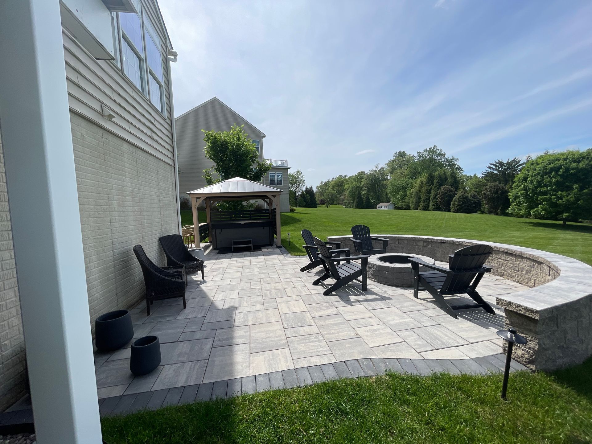 A patio with a fire pit and chairs in front of a house.