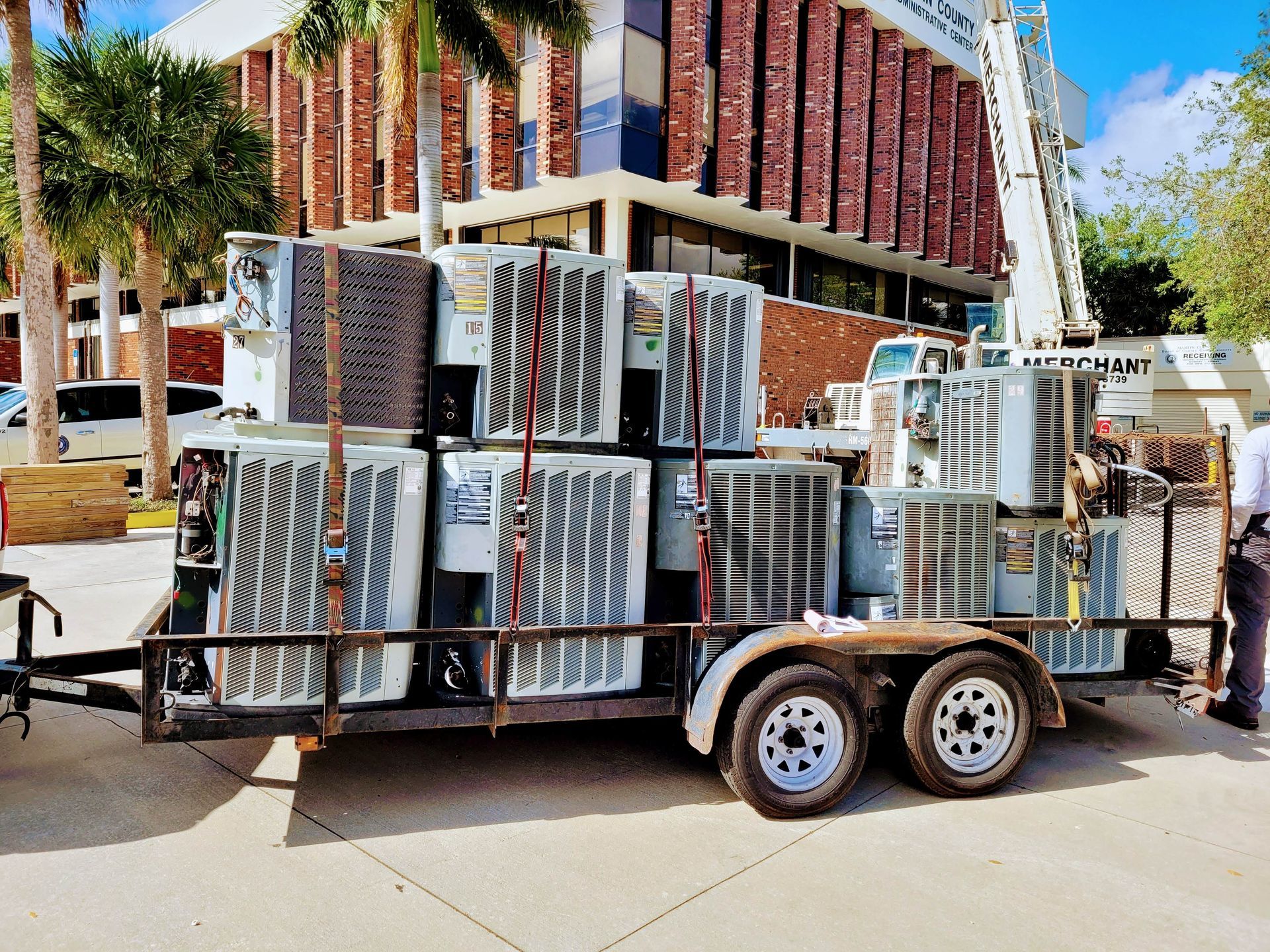 A trailer filled with air conditioners is parked in front of a building.