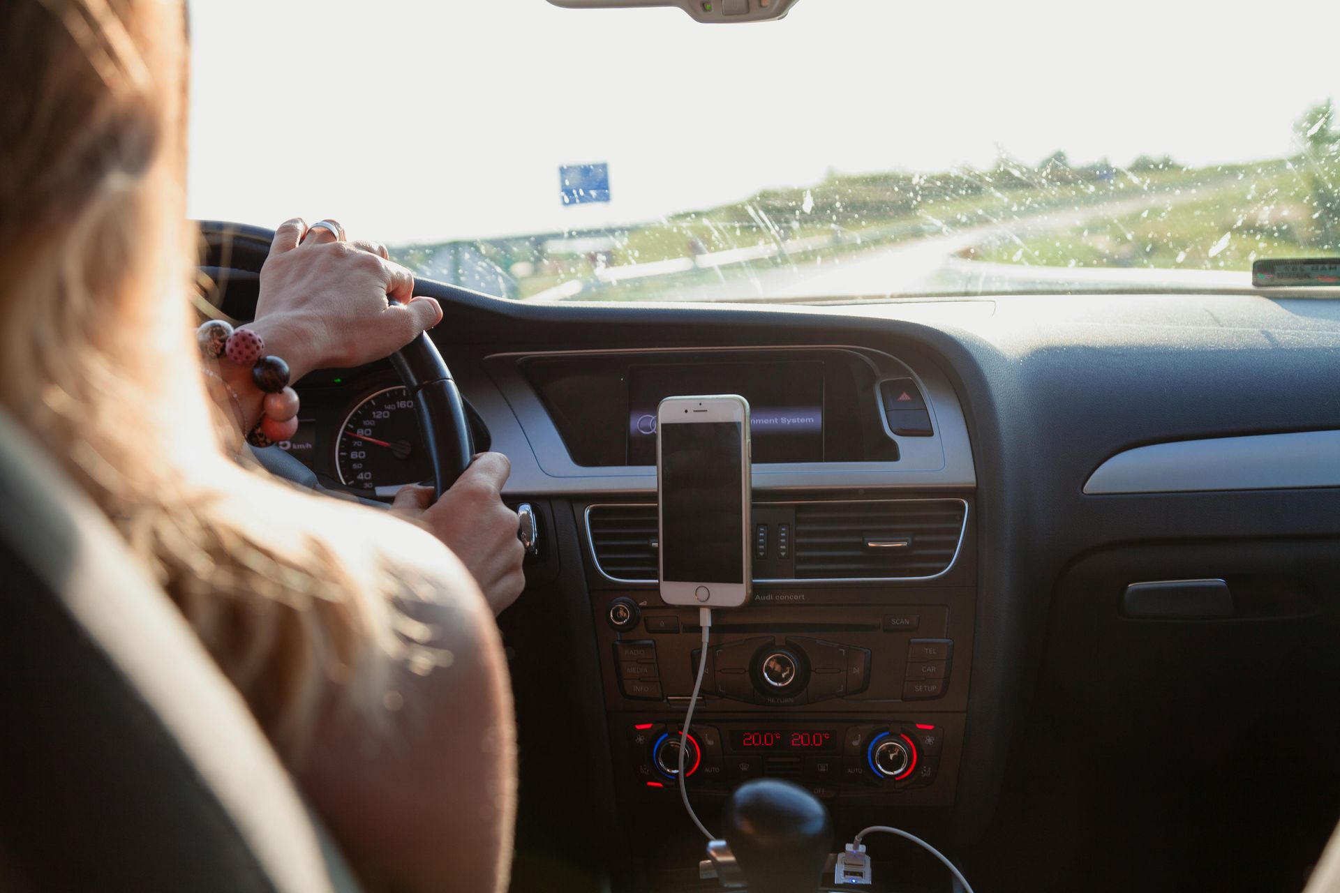 A woman is driving a car with a cell phone plugged into the dashboard.