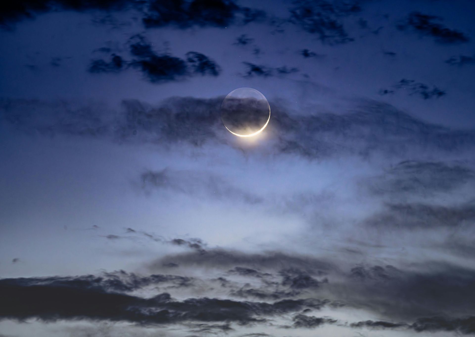 A crescent moon is visible in a cloudy night sky.