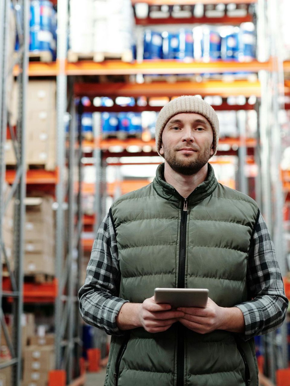 A man is standing in a warehouse holding a tablet.