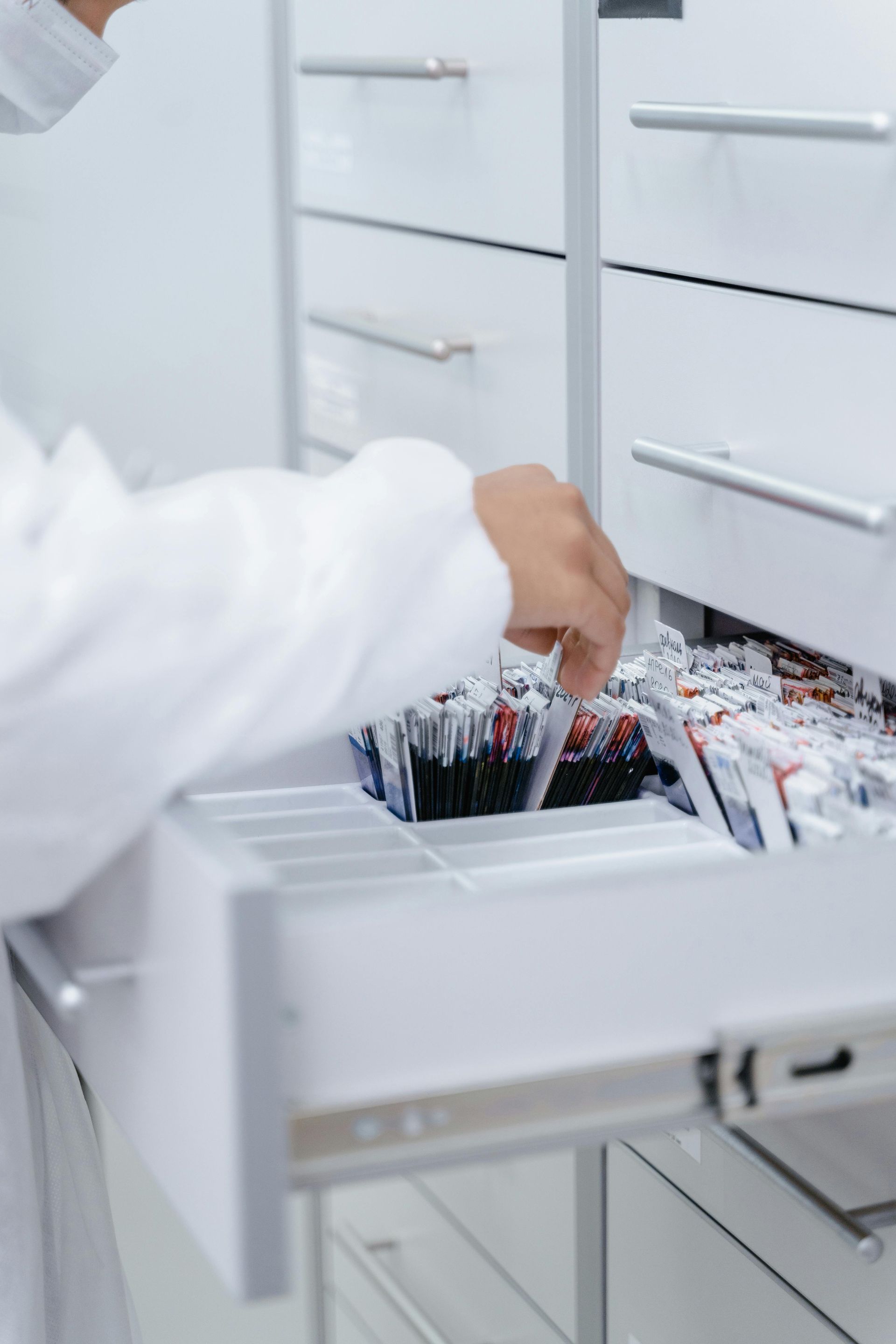 A person in a white coat is taking a pen out of a drawer.