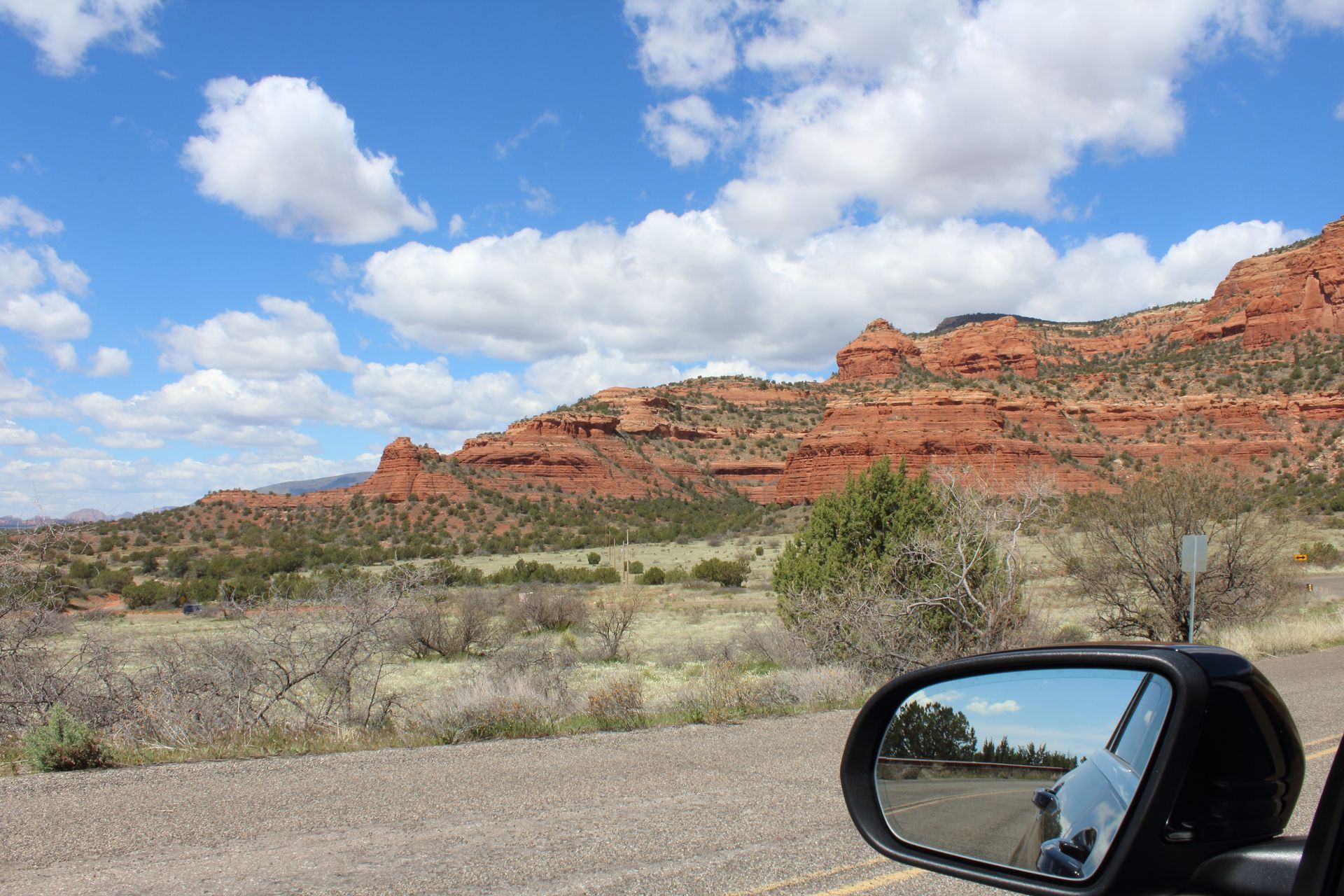 A car 's rear view mirror shows a desert landscape with mountains in the background