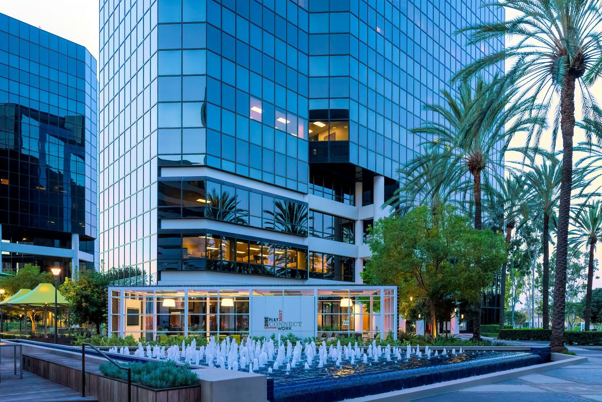 Office buildings with glass facade and palm trees, fountain in the foreground.