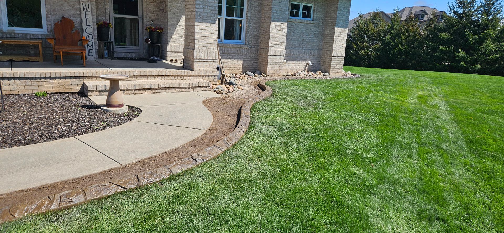 Landscaped front yard with curved stone walkway, mulch bed, and green lawn beside a house