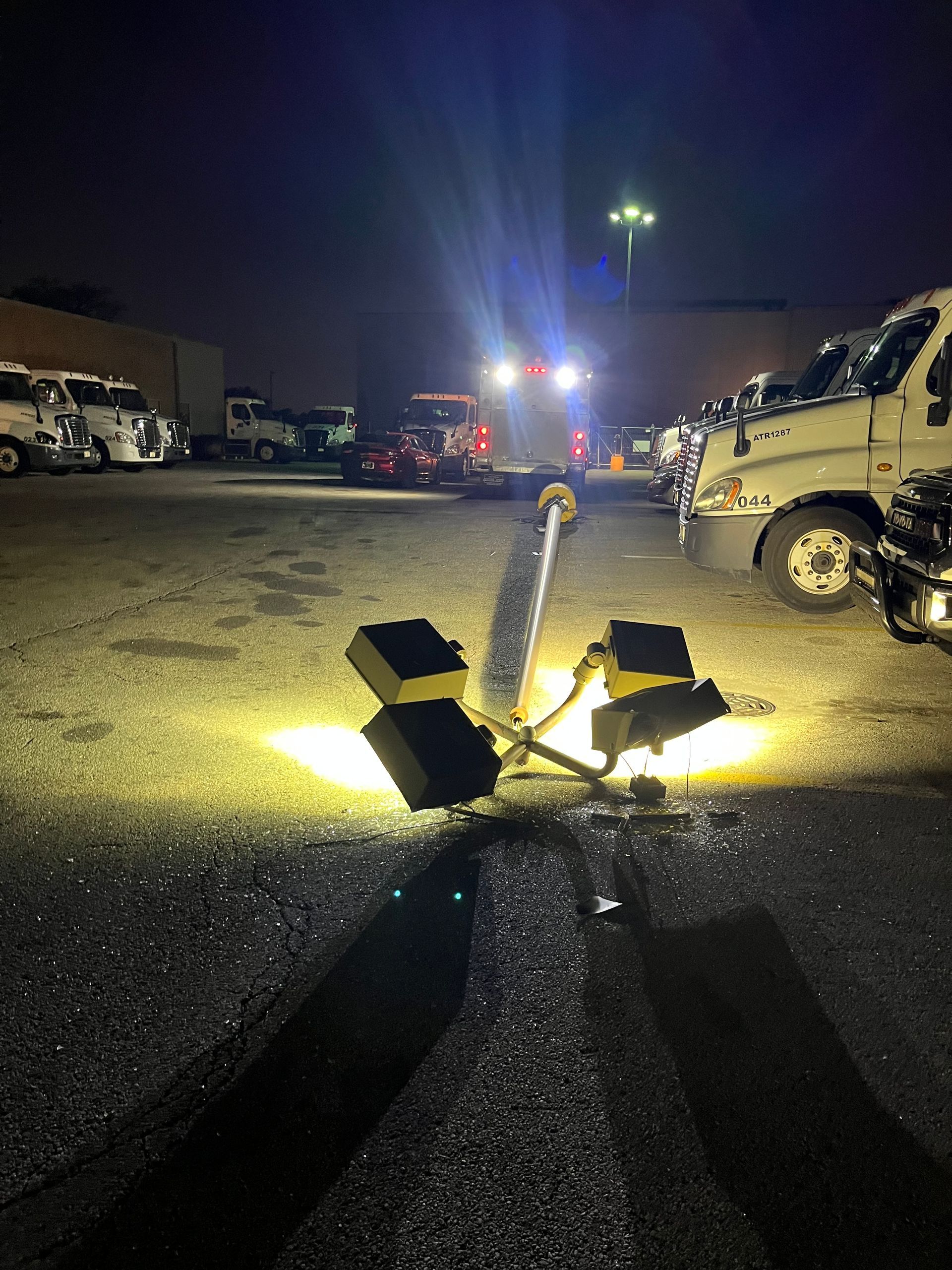Fallen traffic light in a parking lot, illuminated by bright lights. Several trucks are in the background.