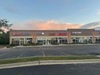 Strip mall with storefronts under a colorful sunset sky. Parking lot in front.