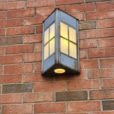 A rectangular, blue outdoor lamp with glass panels mounted on a red brick wall.