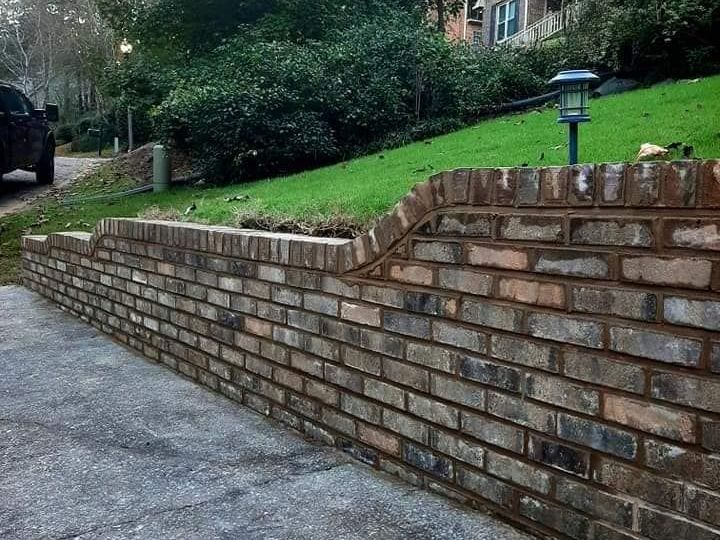 Brick retaining wall bordering a sloping green yard, with a driveway in the foreground.