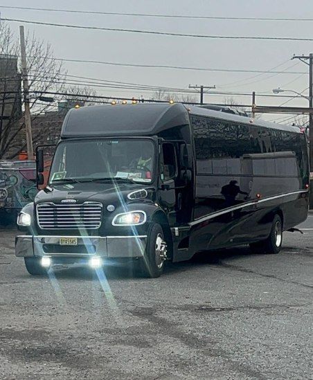 Black party bus parked on a gray surface with overcast sky in background.