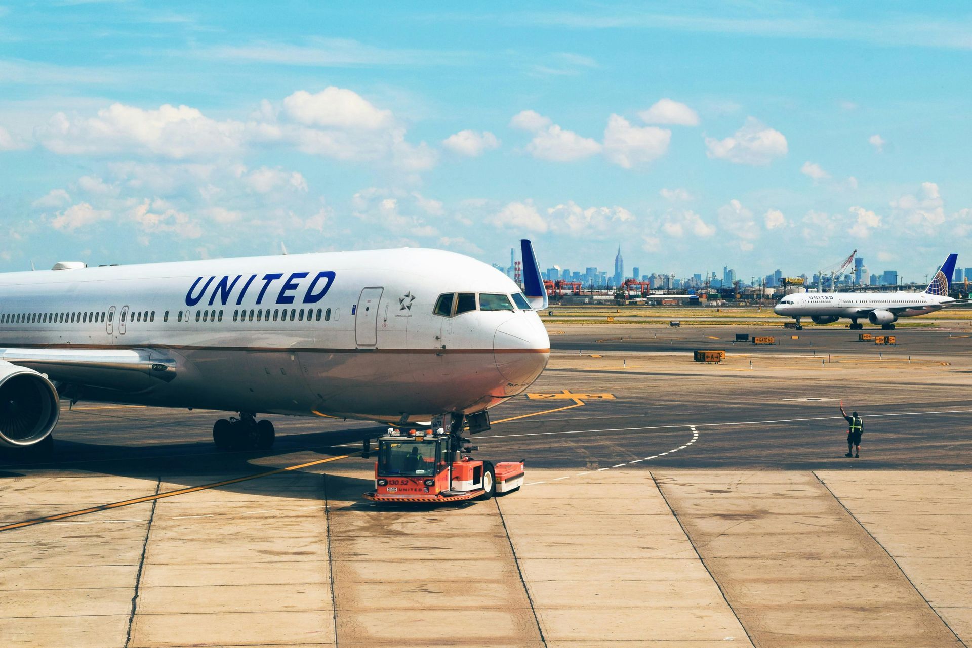 United Airlines plane on the tarmac with a city skyline in the background, blue sky, sunny day.